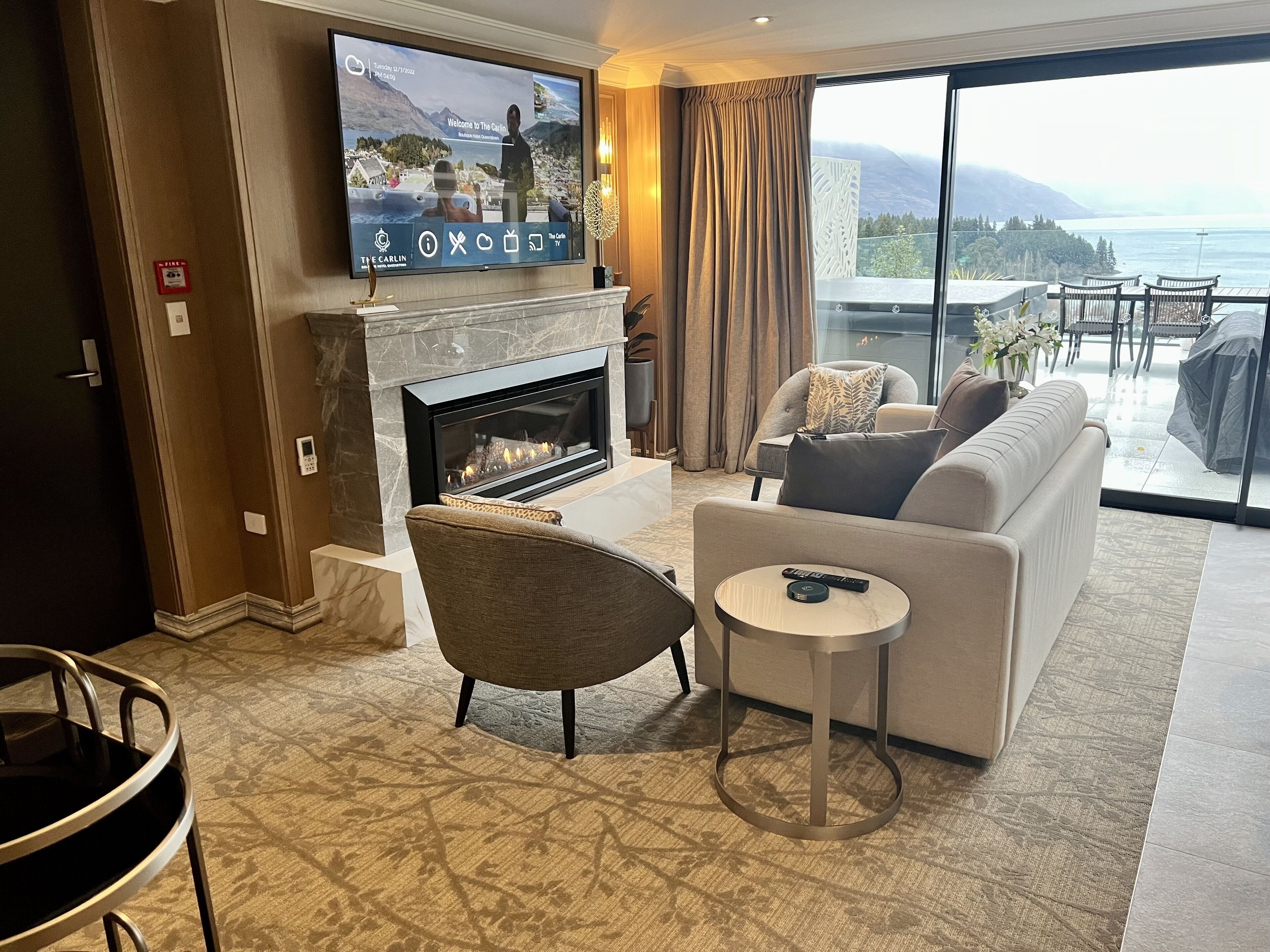 A modern living room with a fireplace, a television mounted on the wall, a sofa, a round coffee table, and a view of the ocean through large windows.