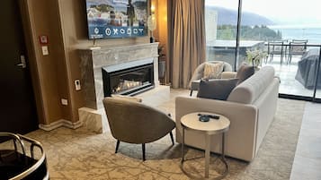 A modern living room with a fireplace, a television mounted on the wall, a sofa, a round coffee table, and a view of the ocean through large windows.