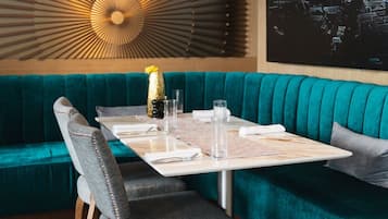 A teal upholstered sofa with a table set for two, featuring a woven placemat, clear glasses, and a decorative bottle.