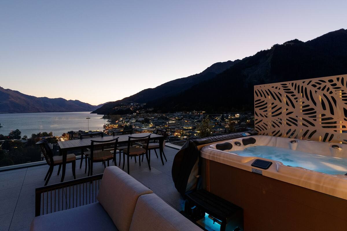 Een hottub met een achtergrond van bladmotieven, met uitzicht op een meer en een stad, met bergen op de achtergrond.
