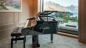 Un piano à queue dans une pièce luxueuse, agrémentée d’un grand lustre, d’un tableau et offrant une vue sur les montagnes.