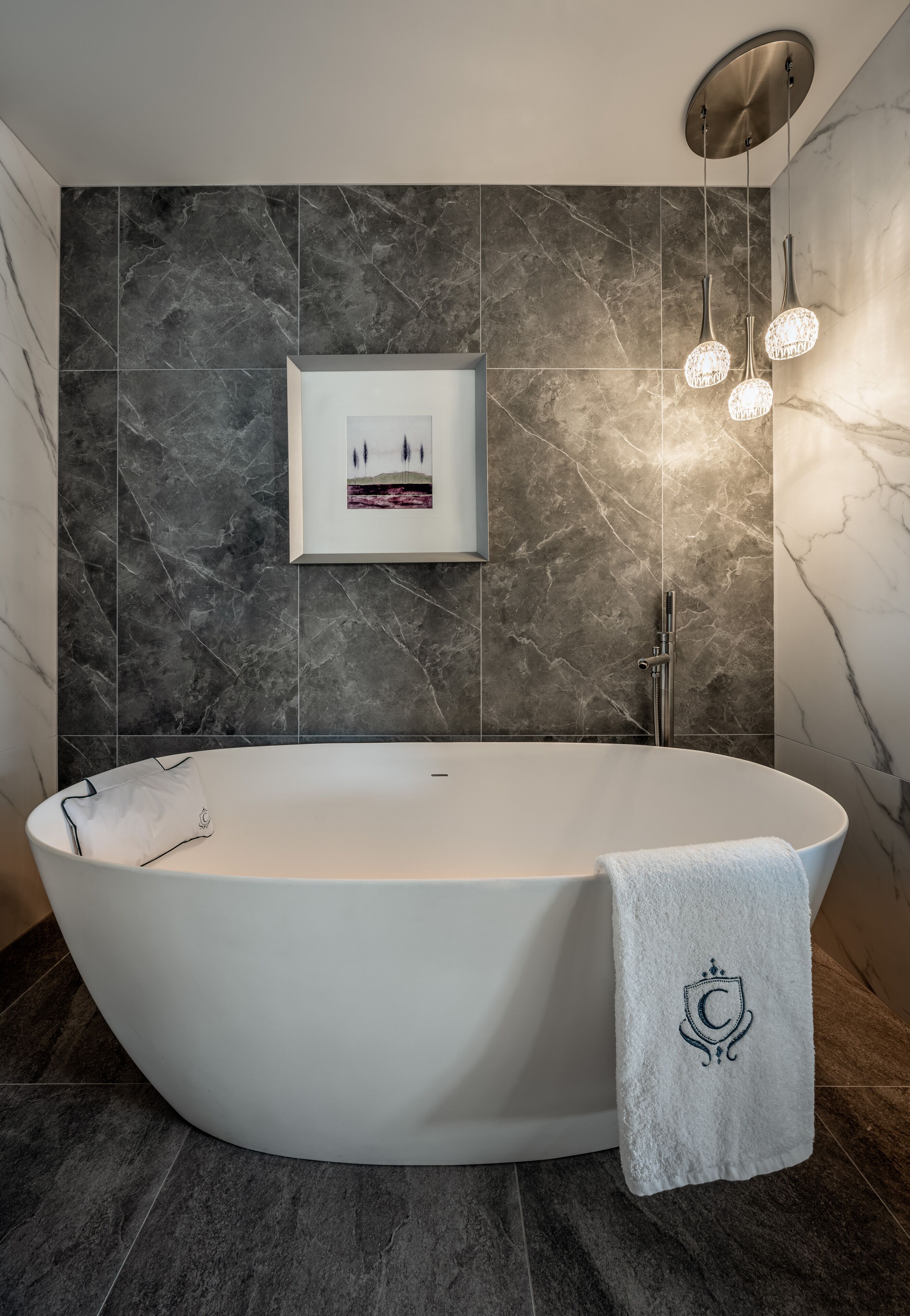 A modern bathroom with a freestanding bathtub, marble walls, and pendant lighting.