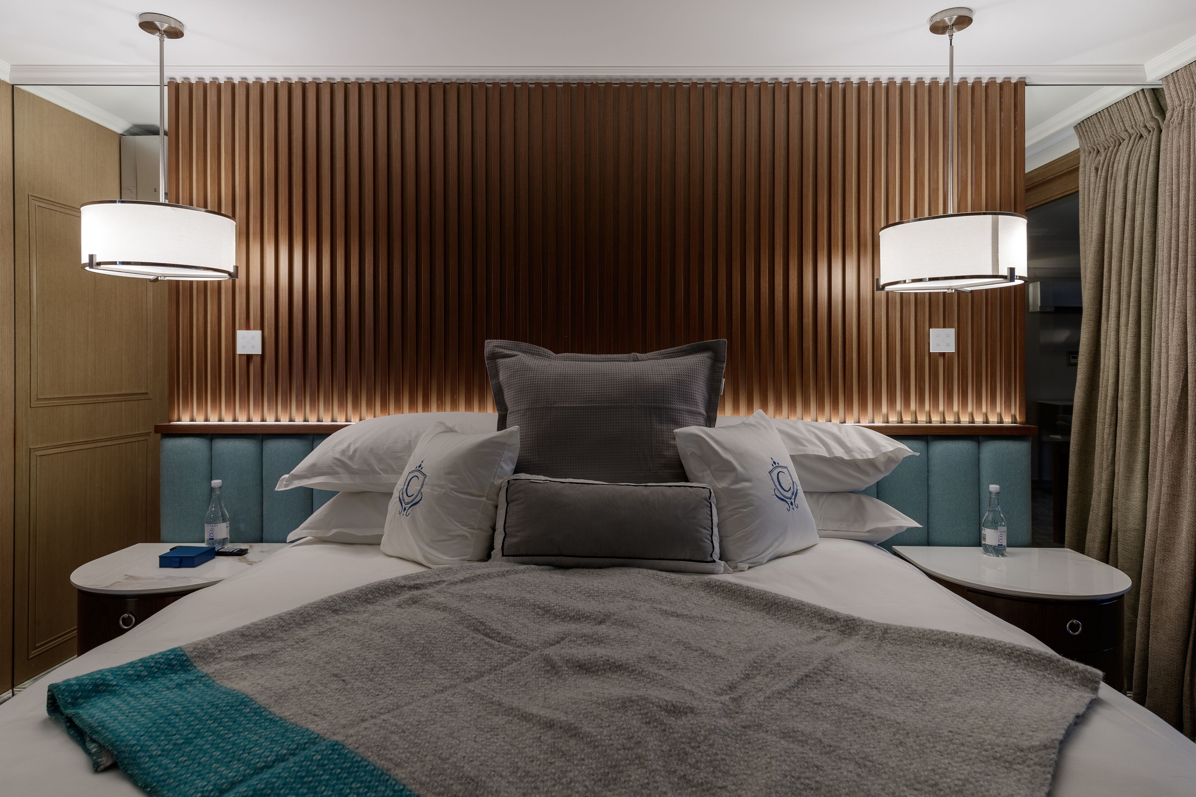 A hotel room with a large bed, two bedside tables, a nightstand, a wall-mounted lamp, and a window with curtains.