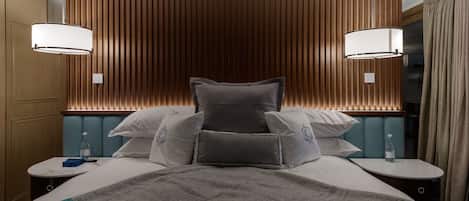 A hotel room with a large bed, two bedside tables, a nightstand, a wall-mounted lamp, and a window with curtains.