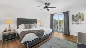 A modern bedroom with a bed, two bedside tables, a ceiling fan, and a view of the outdoors.