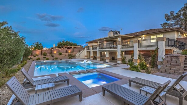 A pool area with lounge chairs, a hot tub, and a building with multiple balconies.