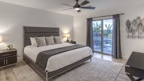 A modern bedroom with a large bed, a ceiling fan, a nightstand with a lamp, and a view of the outdoors through a glass door.