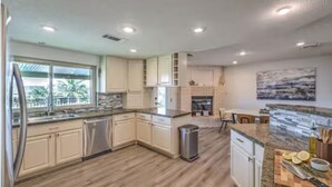 A modern kitchen with light wood flooring, white cabinetry, a central island, and a view of the outdoors.