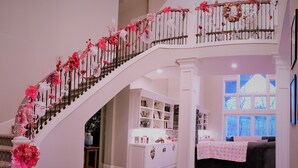 A staircase with pink floral decorations, a white interior, and a view of a living area with a couch and a window.