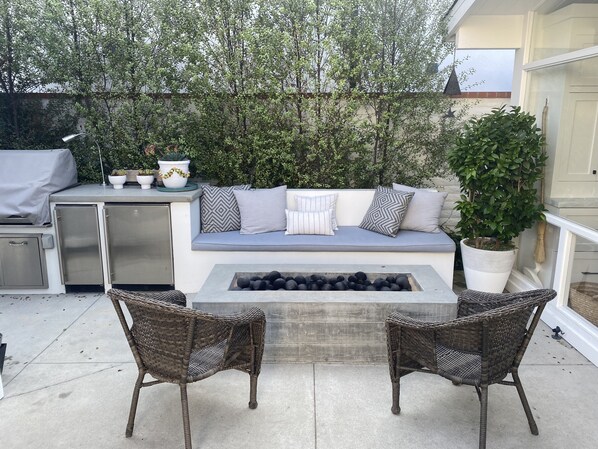 Un patio al aire libre con una zona de estar integrada, una chimenea, sillas de mimbre y plantas en macetas.