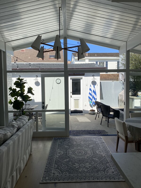 Un patio cubierto con vista a una casa, una zona de comedor con mesa y sillas, y un tapete decorativo grande.
