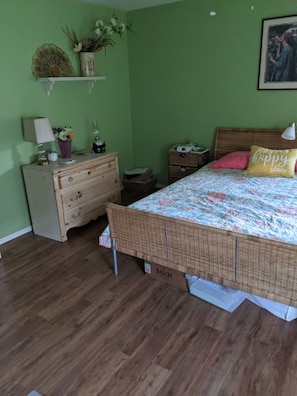 A bedroom with a bed, dresser, nightstand, and a wall-mounted shelf with decorative items.