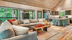 A spacious living room with a large sofa, a coffee table, and a kitchen area with a bar and stools. - Generational Cabin Near Gatlinburg & Dollywood (Sevierville)