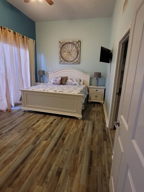 Ein Schlafzimmer mit einem großen Bett, einem Deckenventilator, einem wandmontierten Fernseher und Holzboden.
