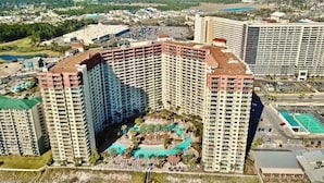 A high-rise hotel with multiple floors, a rooftop pool, and a surrounding landscaped area. - Gorgeous Ground Floor Condo! (Panama City Beach)
