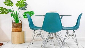 Ein Essbereich mit einem runden Tisch, blaugrünen Stühlen und einer Kübelpflanze mit Monstera-Blättern.