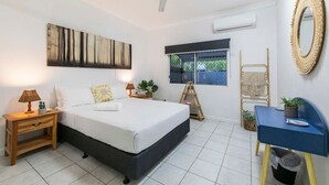 Ein Schlafzimmer mit einem Bett, Nachttischen, einem Schreibtisch, einem Deckenventilator, einem Fenster und einem wandmontierten Spiegel.