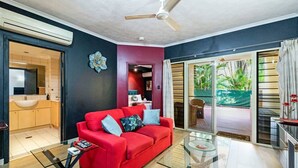 A modern living room with a red sofa, glass coffee table, and a ceiling fan. - Urban Haven ~ Boutique 1BR Apt Near Parap Markets (Parap)
