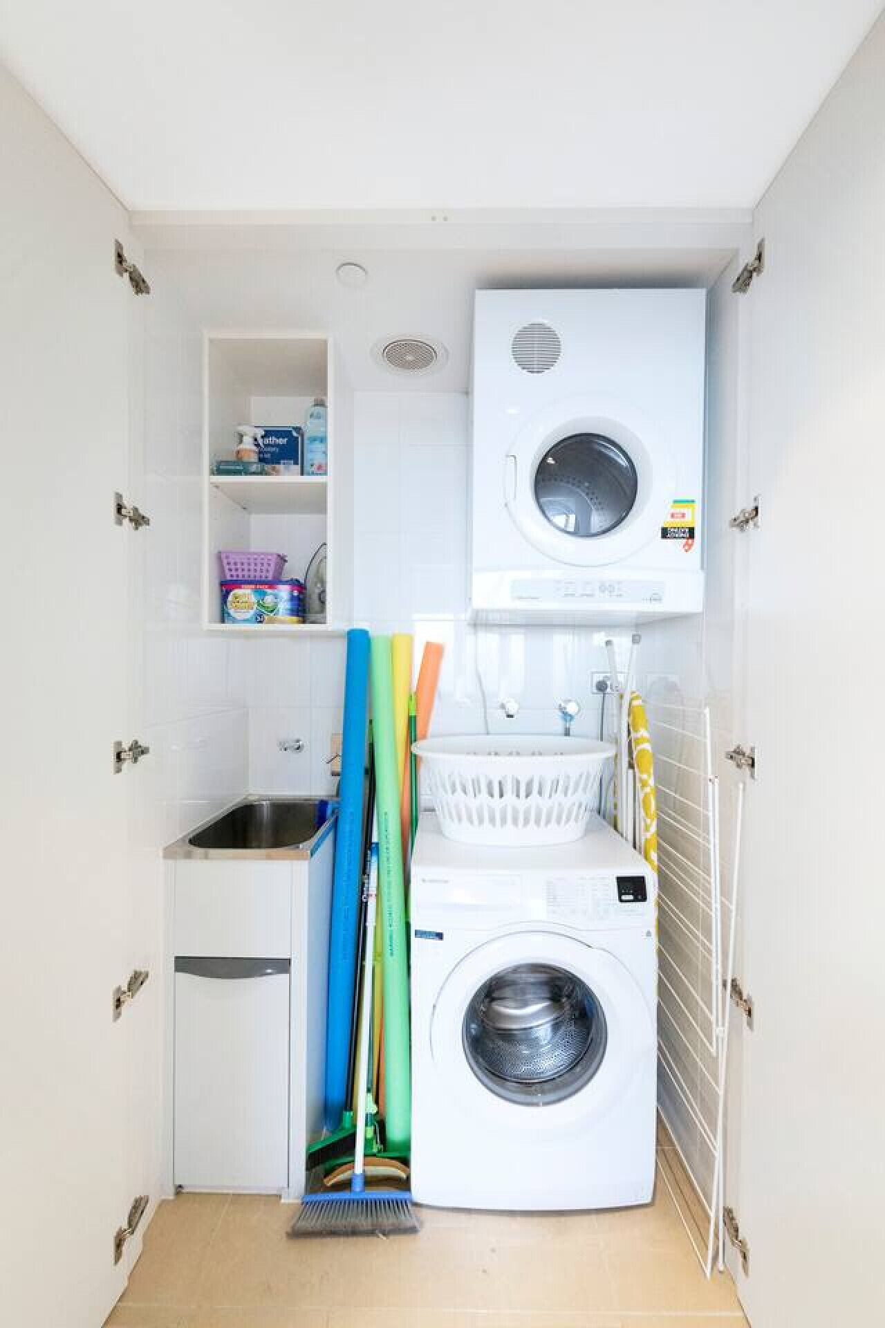 A compact laundry room with a washing machine, a sink, and a drying rack.