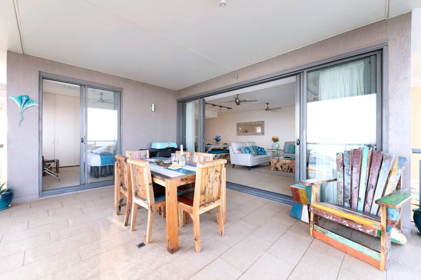 A spacious living area with a wooden dining table and chairs, a colorful chair, and a sliding glass door leading to a balcony.