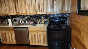 Una cocina con armarios de madera, lavavajillas de acero inoxidable, estufa negra y salpicadero de azulejos.