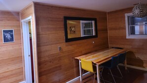 Una habitación con paneles de madera, una mesa de comedor de madera con sillas azules, un cuadro enmarcado y una lámpara en el techo.