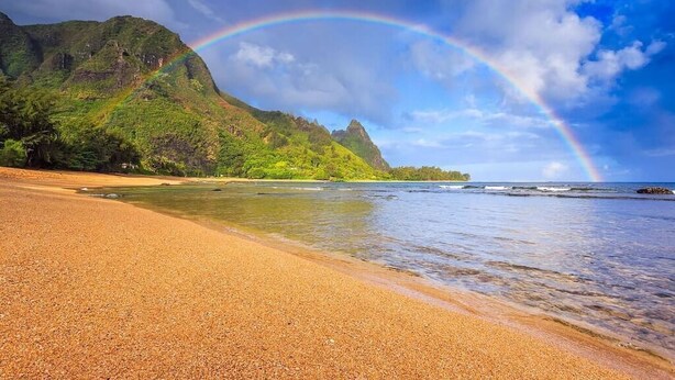A beach with a clear view of a mountain and a rainbow.