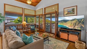 A spacious living room with a large TV, wooden ceiling, and large windows offering a scenic view.