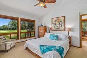 A bedroom with a large bed, a ceiling fan, a view of a golf course, and a painting on the wall.