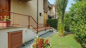 Un edificio residenziale con un balcone, un vialetto in pietra e un vaso grande con fiori rossi.