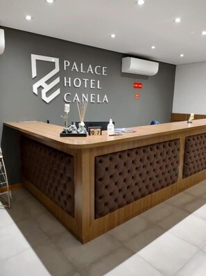 Una recepción en el Hotel Palace Canela con un diseño moderno, un reloj digital y una planta pequeña en el mostrador.