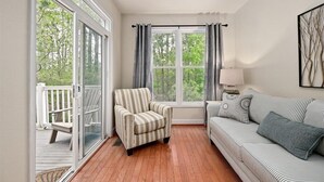 A room with a wooden floor, a striped armchair, a striped sofa, a window with curtains, and a view of greenery outside. - Spacious Townhouse in the GlenRiddle Community (Berlin)