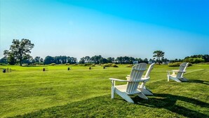 A grassy field with two white Adirondack chairs and a white building in the background. - Spacious Townhouse in the GlenRiddle Community (Berlin)