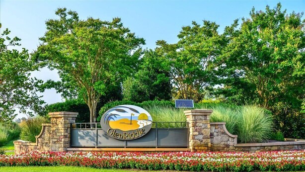 A sign for Glen Riddle with a golf flag logo, surrounded by a stone wall and a flower bed. - Spacious Townhouse in the GlenRiddle Community (Berlin)