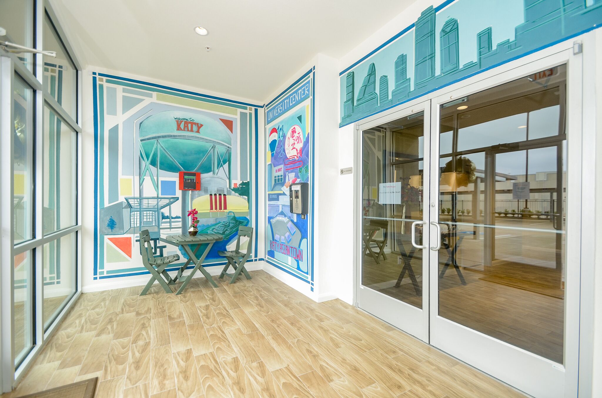 A modern interior with a cityscape mural, a glass door entrance, and a wooden floor.