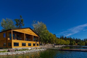 A wooden cabin by a lake with a balcony and large windows.