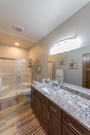 A modern bathroom with a glass shower enclosure, a marble countertop, and wooden cabinets.