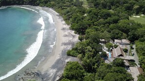 Oversigtsbillede af en kystejendom med strand, frodig vegetation og en golfbane.