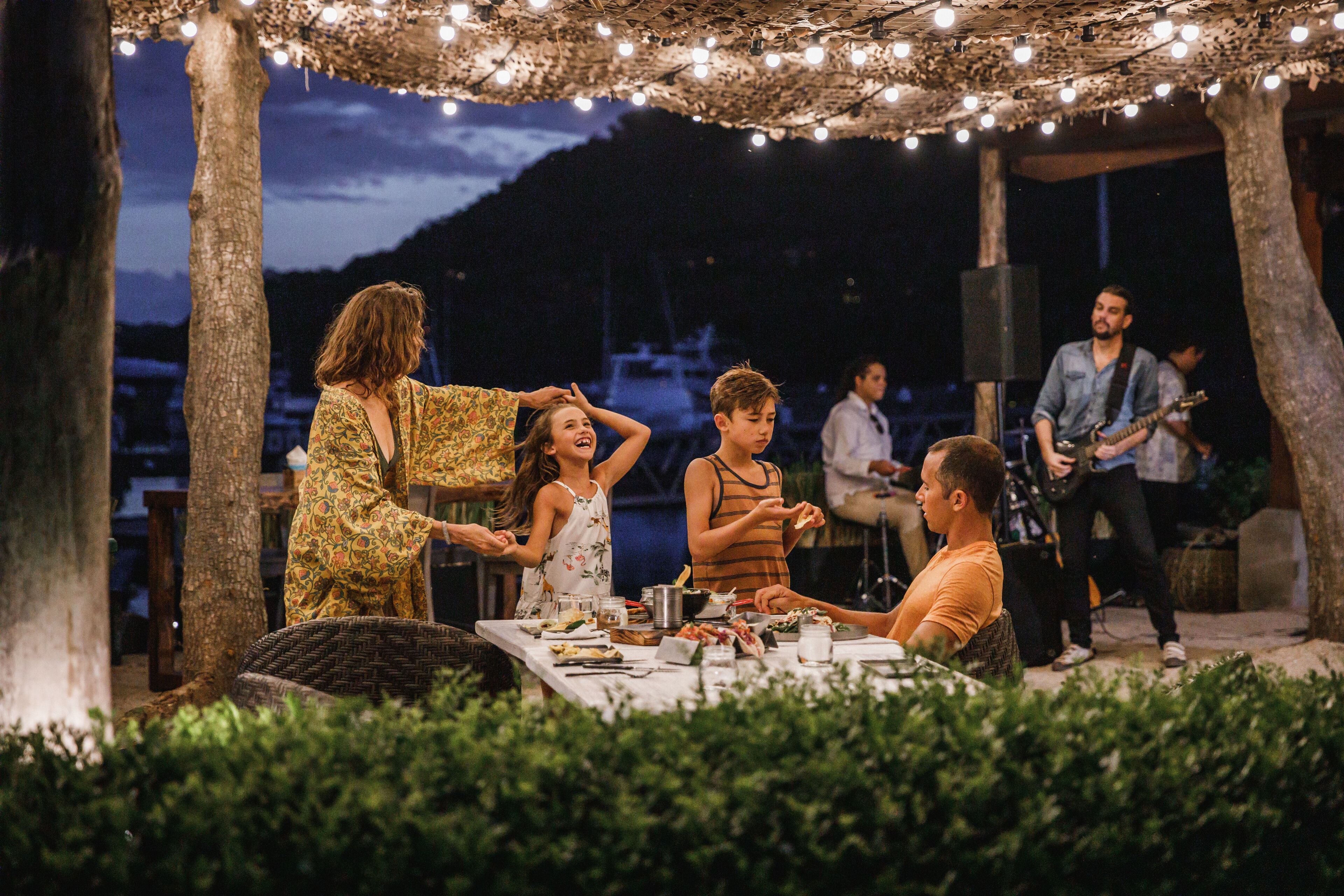Un espace de restauration en plein air, avec des tables et des chaises, entouré d’arbres et illuminé de guirlandes lumineuses.