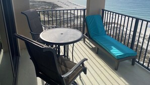 A balcony with a table and chairs, a lounge chair, and a view of the beach and ocean. - Romantic One-bedroom Condo in Orange Beach - Beautiful Gulf-front Views. (Orange Beach)