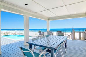Un espacio al aire libre techado con piscina, asientos y vista a la playa.