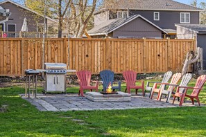 A backyard with a grill, fire pit, and Adirondack chairs.