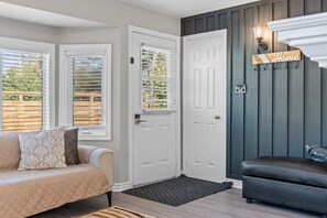 A room with a beige sofa, a dark leather bench, a white door, and a wall-mounted sign that reads 'Home.'