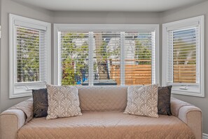 A room with a beige sofa, patterned cushions, and a view through a bay window with blinds. - 🏡 Cozy Family Cottage Retreat | Beach • BBQ • Fire Pit | Sleeps 5 (Innisfil)