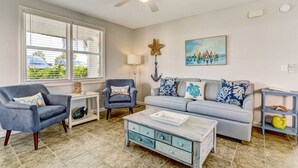 A living room with a grey sofa, two armchairs, a coffee table, and a ceiling fan. - South Beach Cabana Down | Patio | Pool | Across Street from Beach (Fernandina Beach)