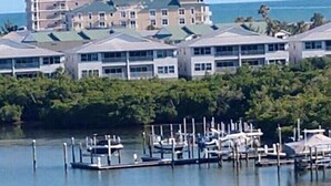 A marina with docked boats, a clear view of the ocean, and a building with multiple floors in the background.