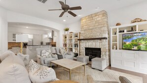 A modern living room with a stone fireplace, white cabinetry, and a flat-screen TV.