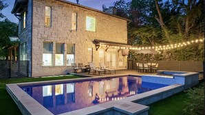 A stone house with a swimming pool, outdoor seating, and string lights.