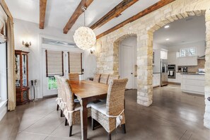 Un comedor amplio con una mesa de madera y sillas de mimbre, un arco de piedra y una cocina moderna al fondo.