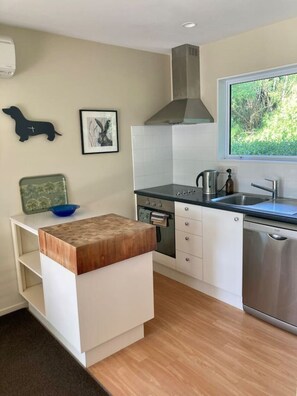 A modern kitchen with white cabinetry, a stainless steel range hood, a built-in oven, and a dishwasher. There is a window providing a view of greenery outside. - `Willowtree` : Where Time Slows & Nature Sings` (Lincoln)